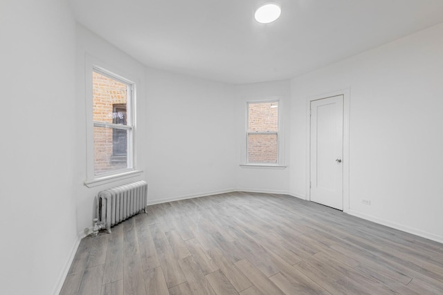 empty room with light wood-type flooring, baseboards, and radiator heating unit