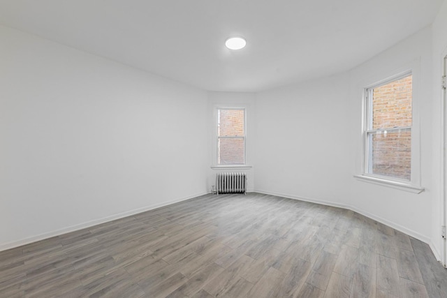 unfurnished room featuring radiator heating unit, baseboards, and wood finished floors