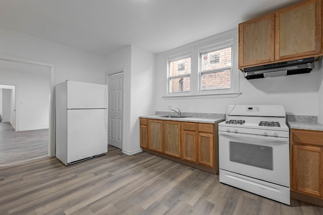 kitchen with white appliances, light wood finished floors, a sink, light countertops, and under cabinet range hood