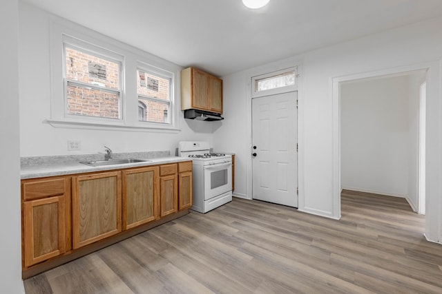 kitchen featuring light wood-style flooring, a sink, under cabinet range hood, light countertops, and white range with gas stovetop