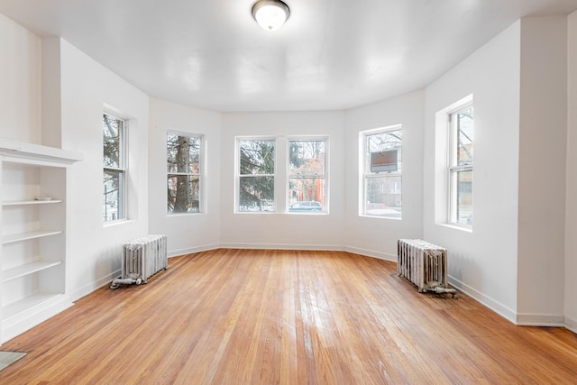 unfurnished dining area featuring built in features, light wood-style flooring, radiator, and baseboards