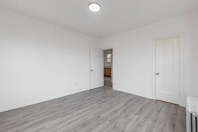 unfurnished room with radiator heating unit, baseboards, and light wood finished floors