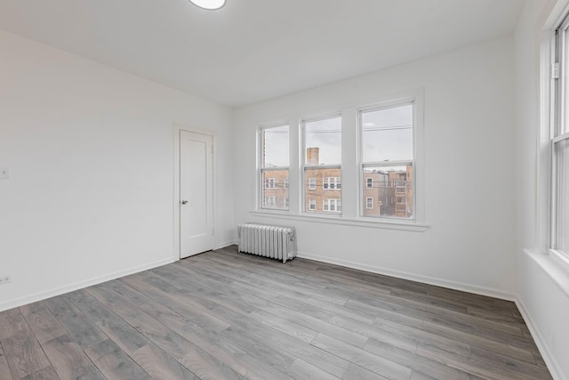 empty room with radiator heating unit, wood finished floors, and baseboards