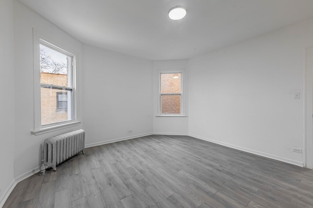 unfurnished room featuring radiator heating unit, wood finished floors, and baseboards