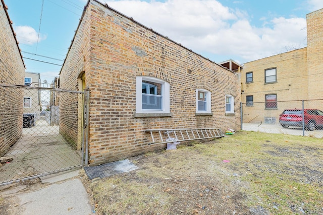 view of side of home featuring a gate, fence, and brick siding