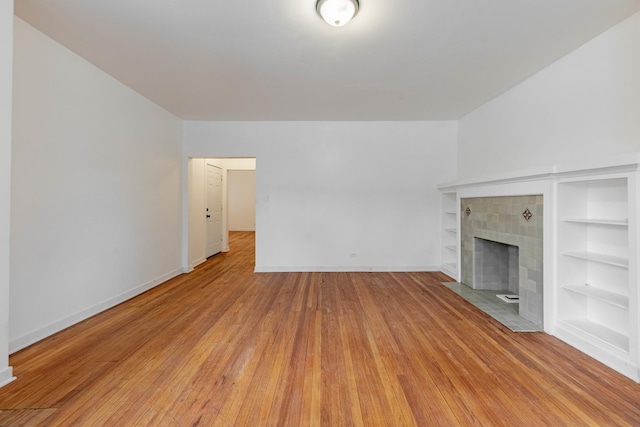 unfurnished living room with built in features, light wood-type flooring, baseboards, and a tile fireplace