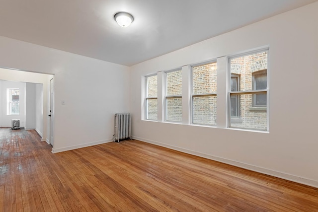 unfurnished room featuring hardwood / wood-style flooring, radiator, and baseboards