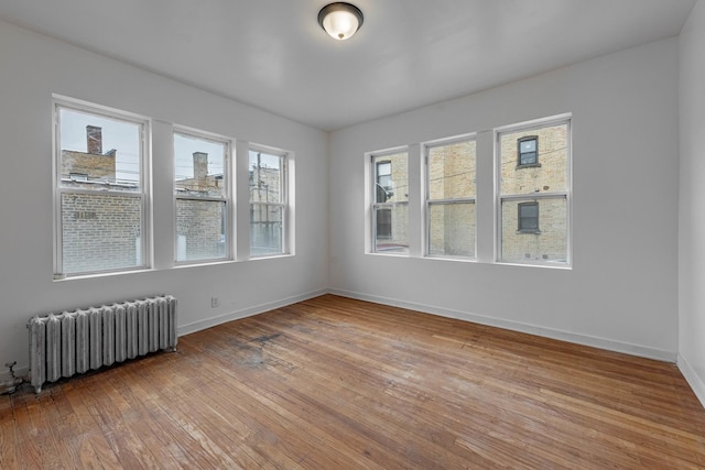 spare room with baseboards, radiator heating unit, and light wood-style floors