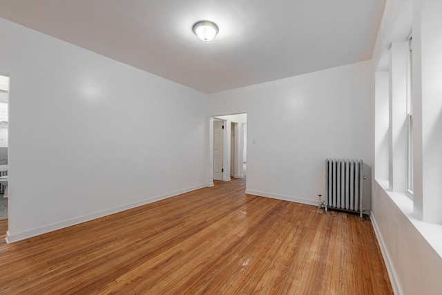 unfurnished room featuring radiator, light wood-style floors, and baseboards