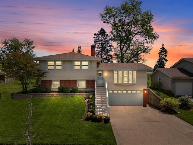 tri-level home with concrete driveway, a lawn, an attached garage, a chimney, and brick siding