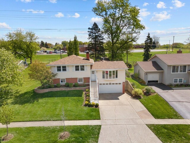 split level home featuring a front lawn, concrete driveway, an attached garage, stairs, and a chimney