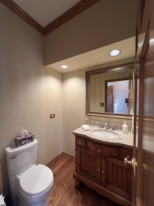 half bathroom with crown molding, baseboards, toilet, wood finished floors, and vanity