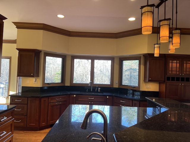 kitchen featuring dark stone countertops, ornamental molding, light wood finished floors, and a sink