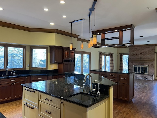 kitchen featuring a warming drawer, wood finished floors, a center island with sink, and a sink