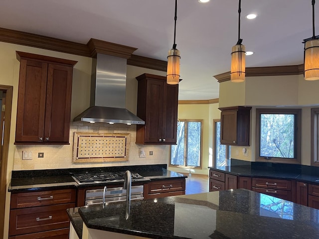 kitchen with crown molding, decorative light fixtures, decorative backsplash, dark stone countertops, and wall chimney exhaust hood