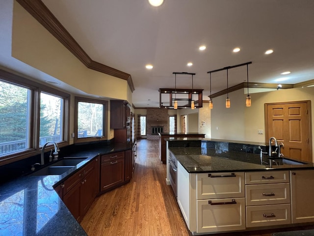 kitchen with a sink, open floor plan, dark stone countertops, and ornamental molding