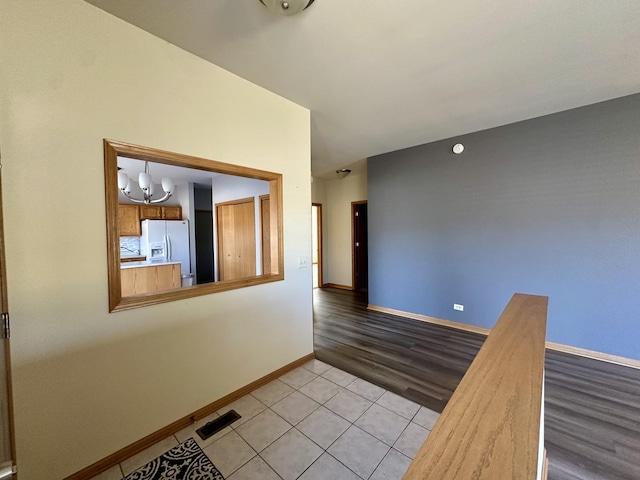 empty room with light tile patterned floors, a notable chandelier, visible vents, and baseboards