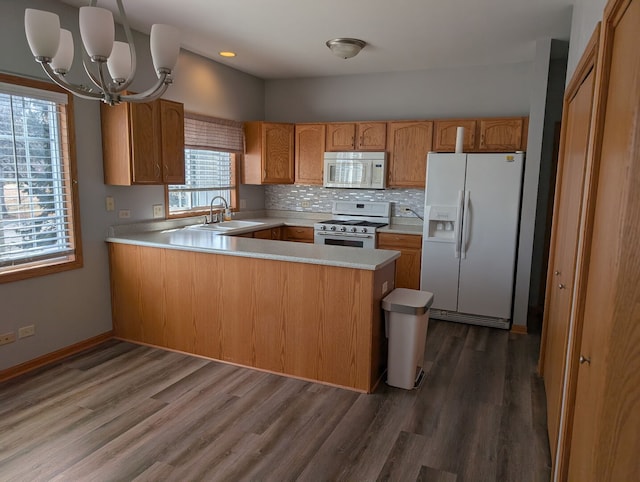 kitchen featuring white appliances, dark wood finished floors, a peninsula, a sink, and light countertops