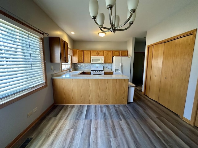 kitchen featuring light countertops, decorative backsplash, a peninsula, an inviting chandelier, and white appliances