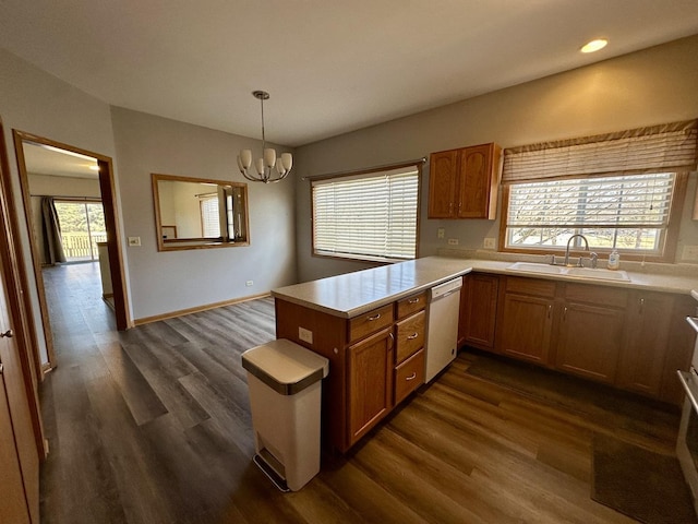 kitchen with dark wood finished floors, a peninsula, a sink, dishwasher, and a chandelier