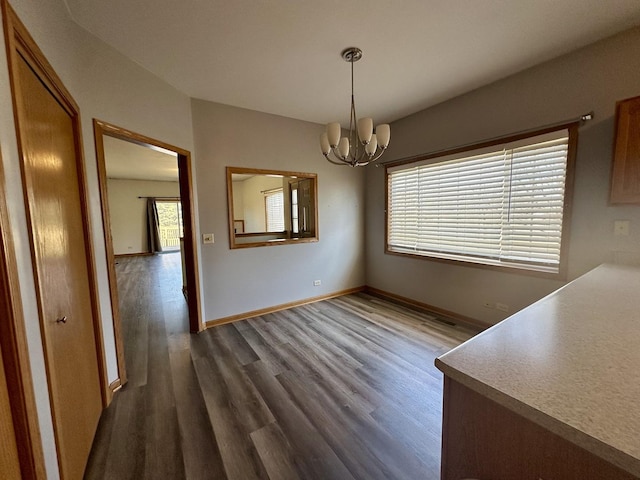 unfurnished dining area featuring dark wood-style floors, baseboards, and an inviting chandelier