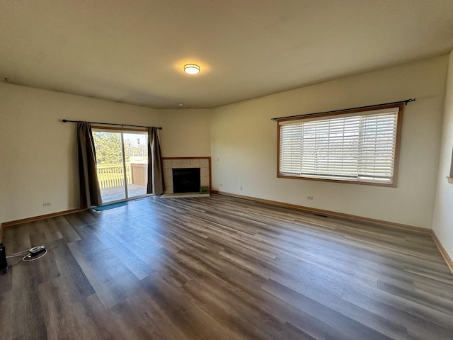 unfurnished living room featuring a tiled fireplace, wood finished floors, and baseboards