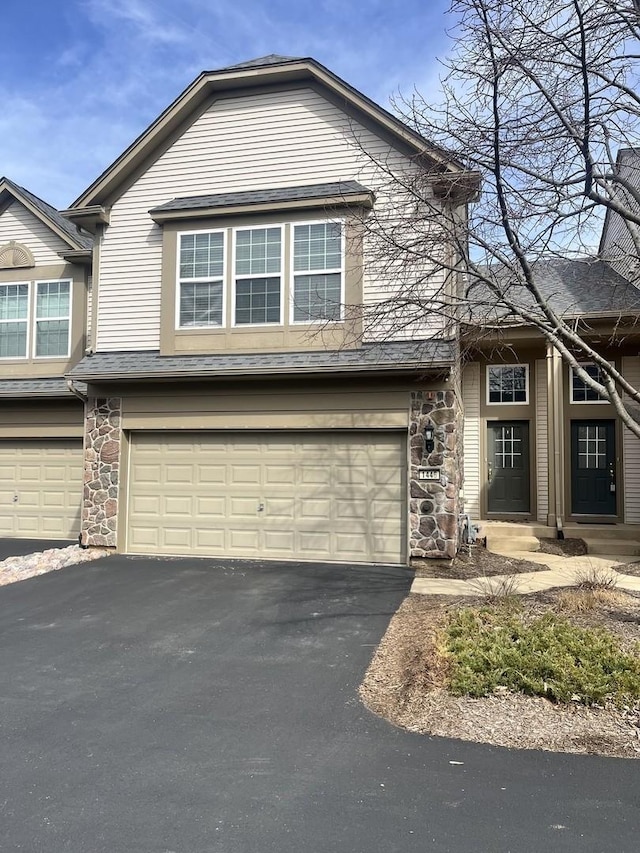 view of front facade featuring stone siding, aphalt driveway, and an attached garage