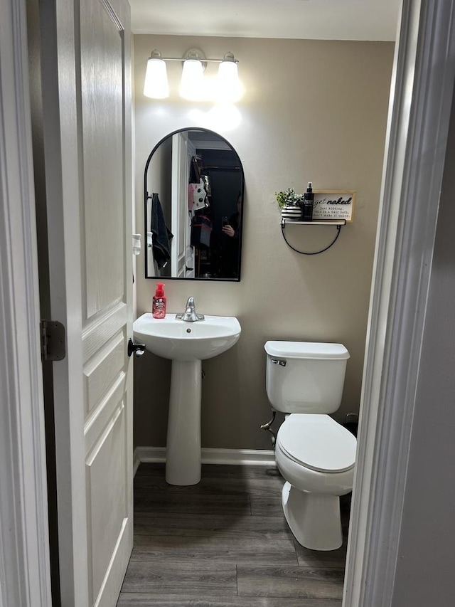 half bath with toilet, wood finished floors, baseboards, and a sink