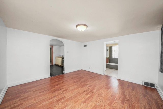 spare room featuring arched walkways, visible vents, baseboards, and wood finished floors