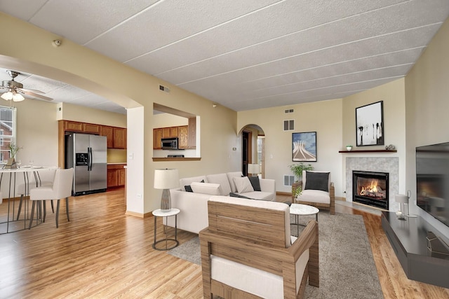 living area featuring ceiling fan, visible vents, arched walkways, light wood-type flooring, and a glass covered fireplace