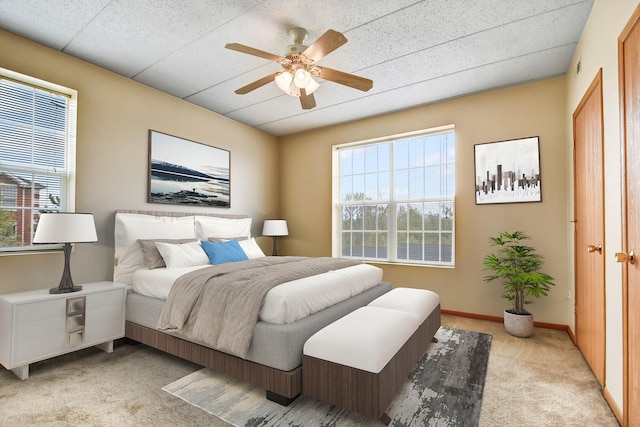 bedroom with baseboards, multiple windows, light carpet, and a ceiling fan