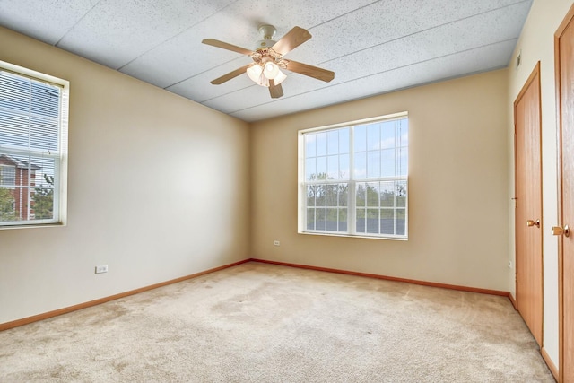 spare room featuring light colored carpet, a ceiling fan, and baseboards