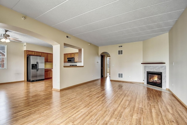 unfurnished living room featuring a fireplace with flush hearth, a ceiling fan, light wood finished floors, and visible vents