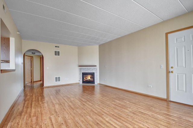 unfurnished living room featuring light wood-style floors, baseboards, a tile fireplace, and visible vents