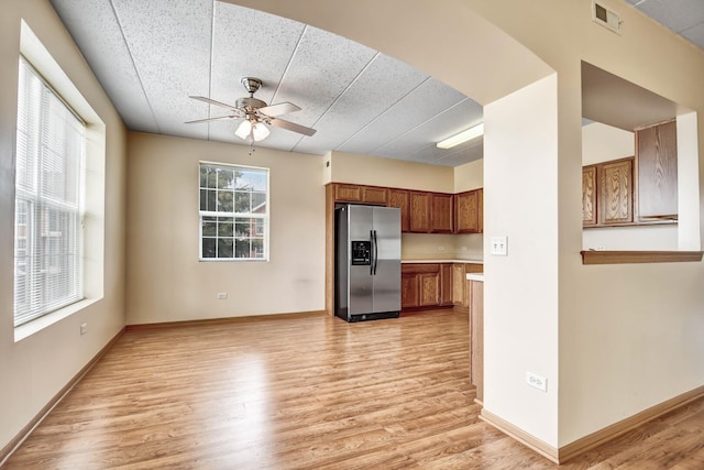 kitchen with brown cabinetry, visible vents, ceiling fan, stainless steel refrigerator with ice dispenser, and light wood-style flooring