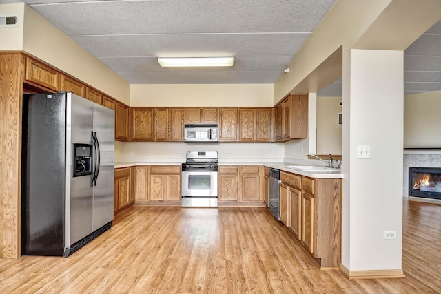 kitchen with appliances with stainless steel finishes, a sink, light countertops, a tiled fireplace, and light wood-style flooring