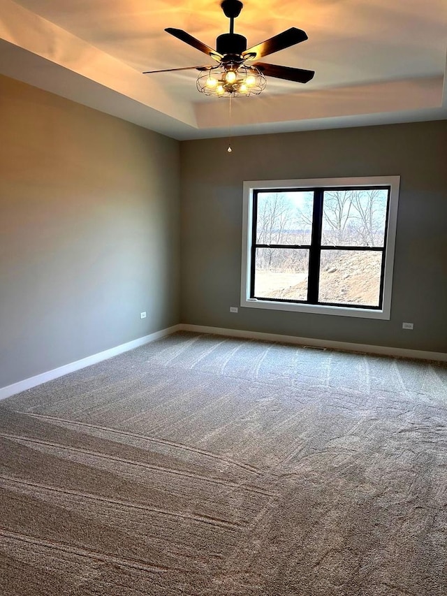 carpeted spare room with baseboards, a raised ceiling, and ceiling fan