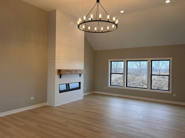 unfurnished living room featuring high vaulted ceiling, wood finished floors, a fireplace, baseboards, and a chandelier