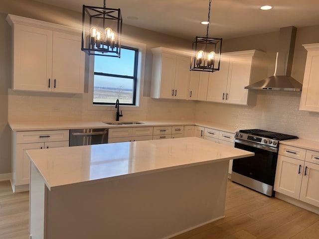 kitchen featuring a sink, light countertops, appliances with stainless steel finishes, wall chimney range hood, and a chandelier