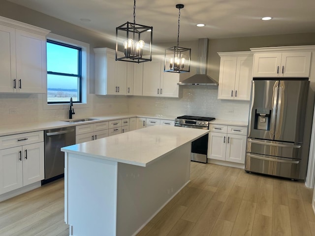 kitchen featuring a sink, stainless steel appliances, light countertops, white cabinetry, and wall chimney range hood
