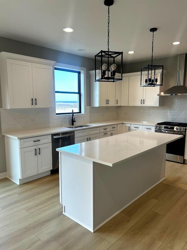 kitchen featuring wall chimney range hood, light wood-style floors, appliances with stainless steel finishes, and a center island