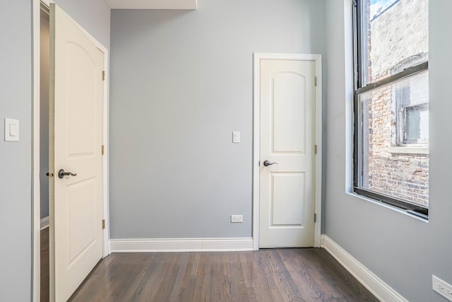 unfurnished bedroom with multiple windows, baseboards, and dark wood-style flooring