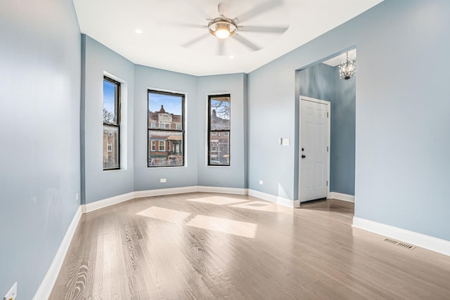 empty room with visible vents, baseboards, wood finished floors, and ceiling fan with notable chandelier