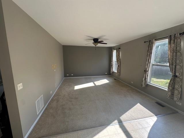 spare room with carpet flooring, a ceiling fan, visible vents, and baseboards