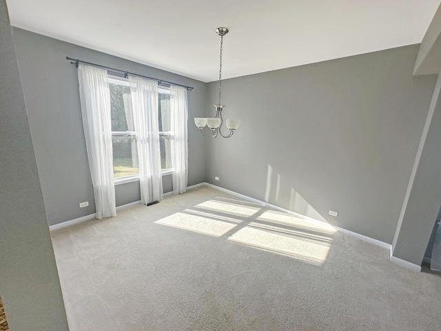 carpeted empty room featuring baseboards and an inviting chandelier