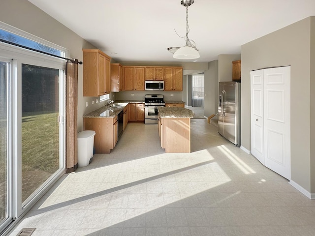 kitchen featuring a center island, light stone counters, hanging light fixtures, stainless steel appliances, and a sink