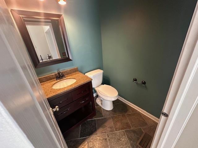 bathroom with vanity, stone finish floor, toilet, and baseboards