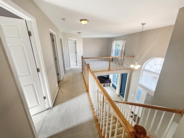 hall featuring an inviting chandelier, an upstairs landing, light colored carpet, and baseboards