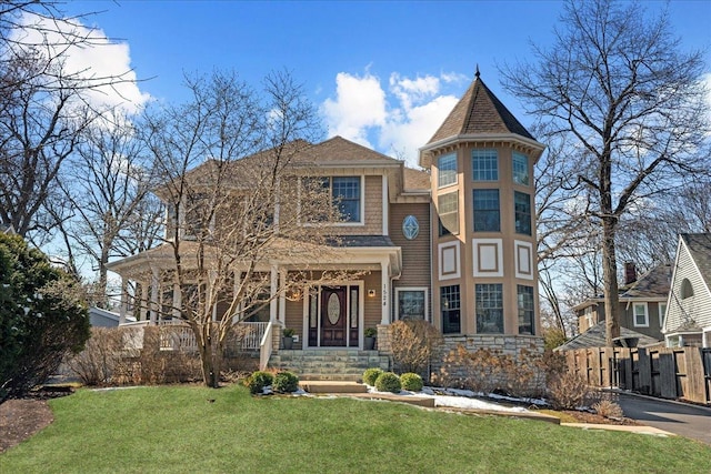 victorian house featuring a front lawn, fence, stone siding, and a shingled roof