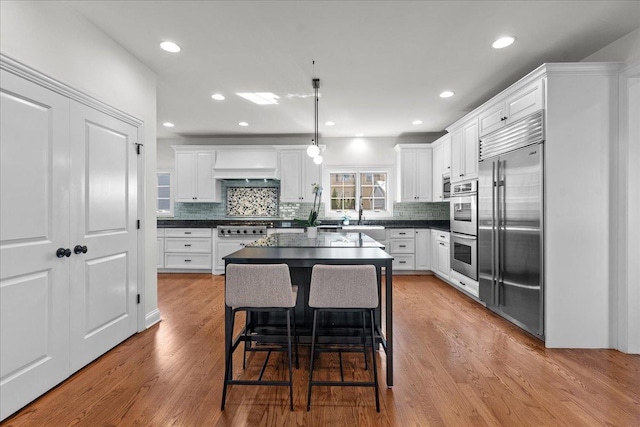 kitchen with white cabinetry, dark countertops, custom range hood, and stainless steel appliances
